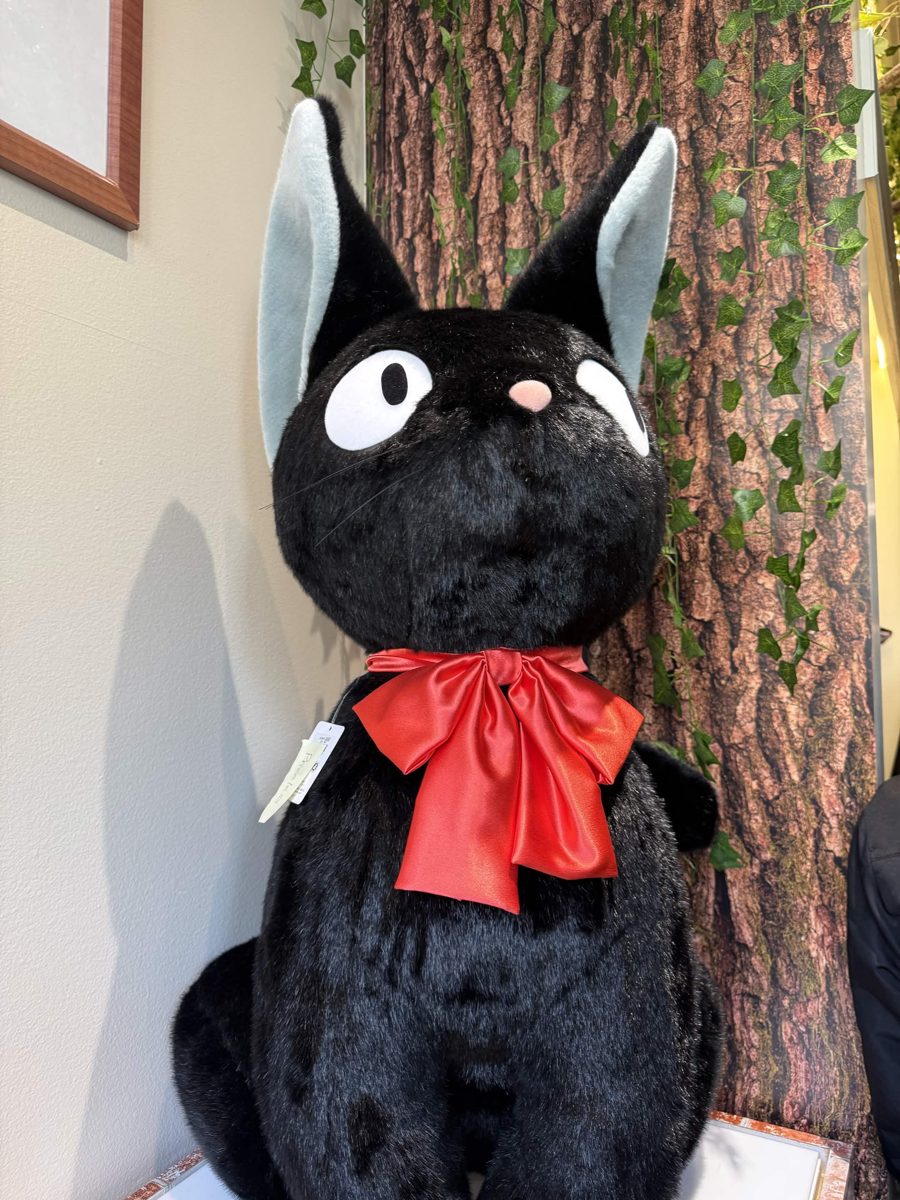 A giant black cat plush with a red bow at a Studio Ghibli pop-up