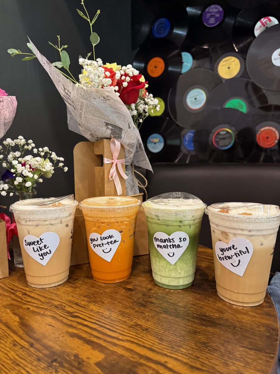 Four iced drinks with pun-filled heart labels at a café with a vinyl record wall