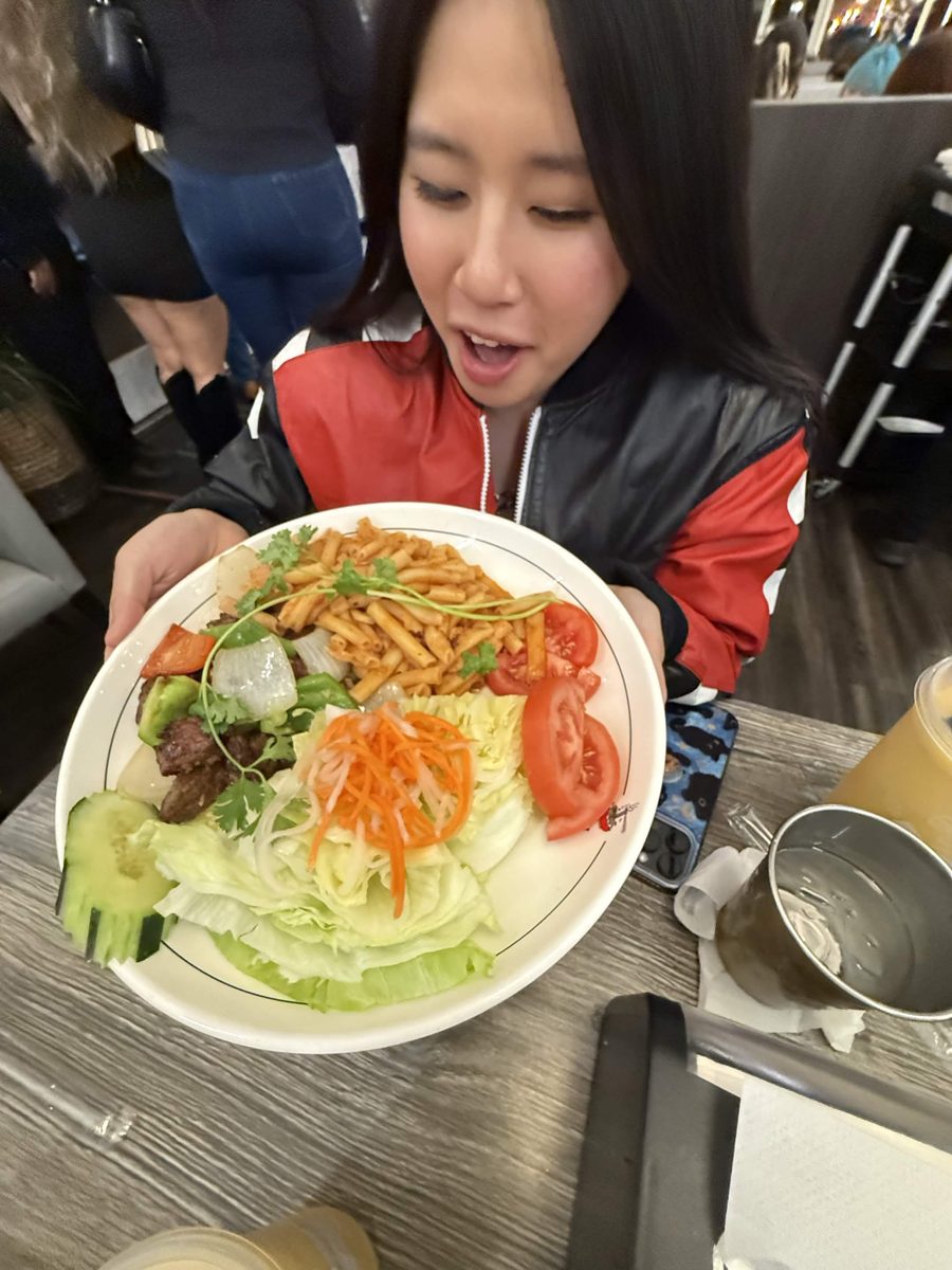 Lyanna excitedly holding up a plate of shaking beef, pasta and salad